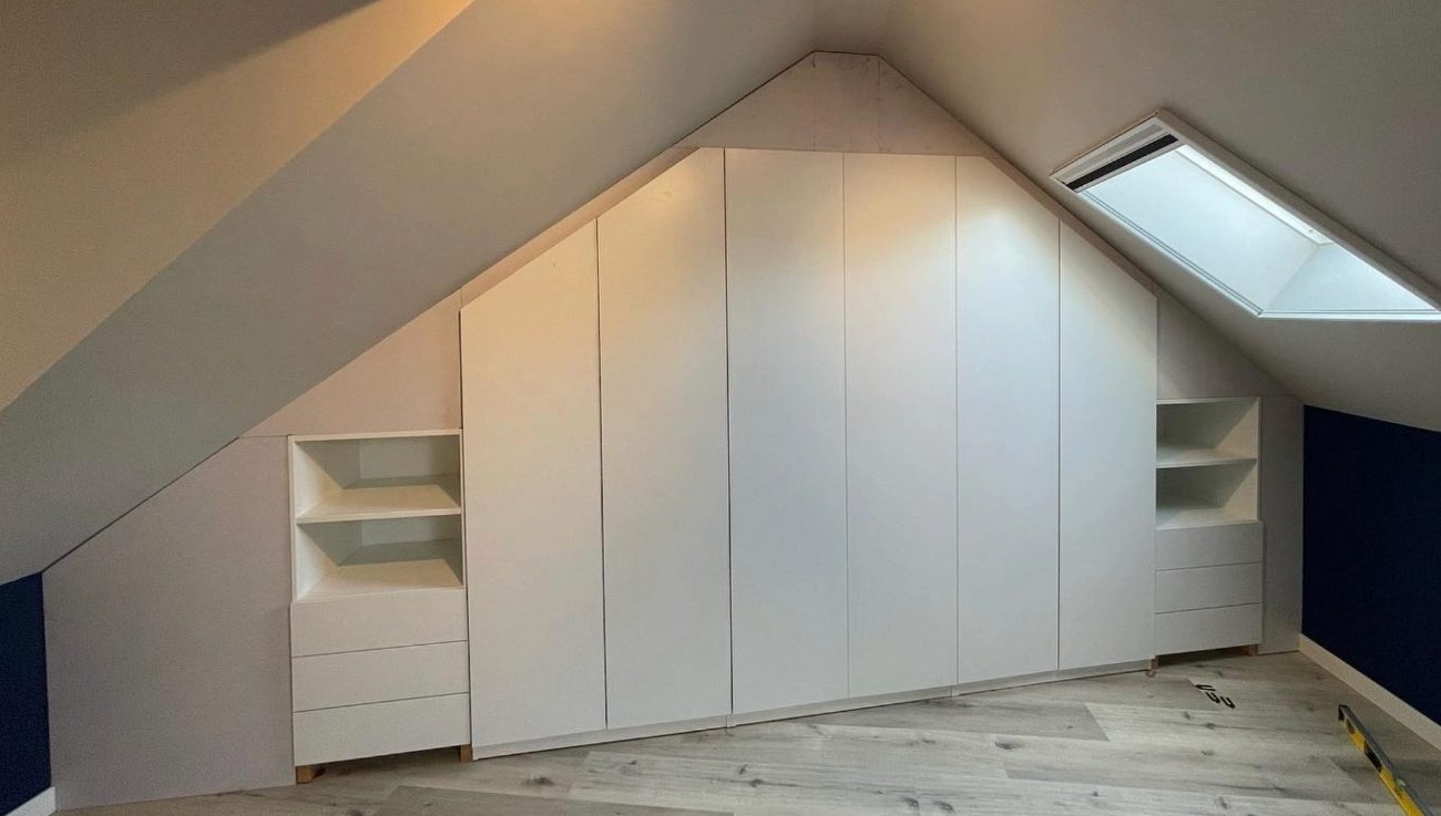 Afgewerkte inbouwkasten met witte fronten onder een schuin zolderdak